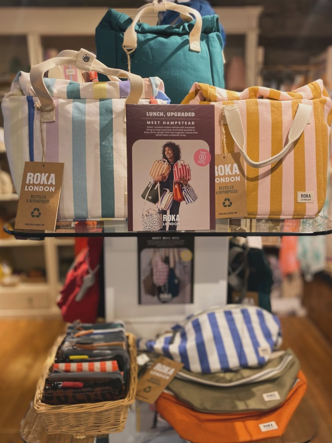 ROKA London striped bags and pouches displayed on a glass shelf inside The Gift Horse, with more of the shop behind.