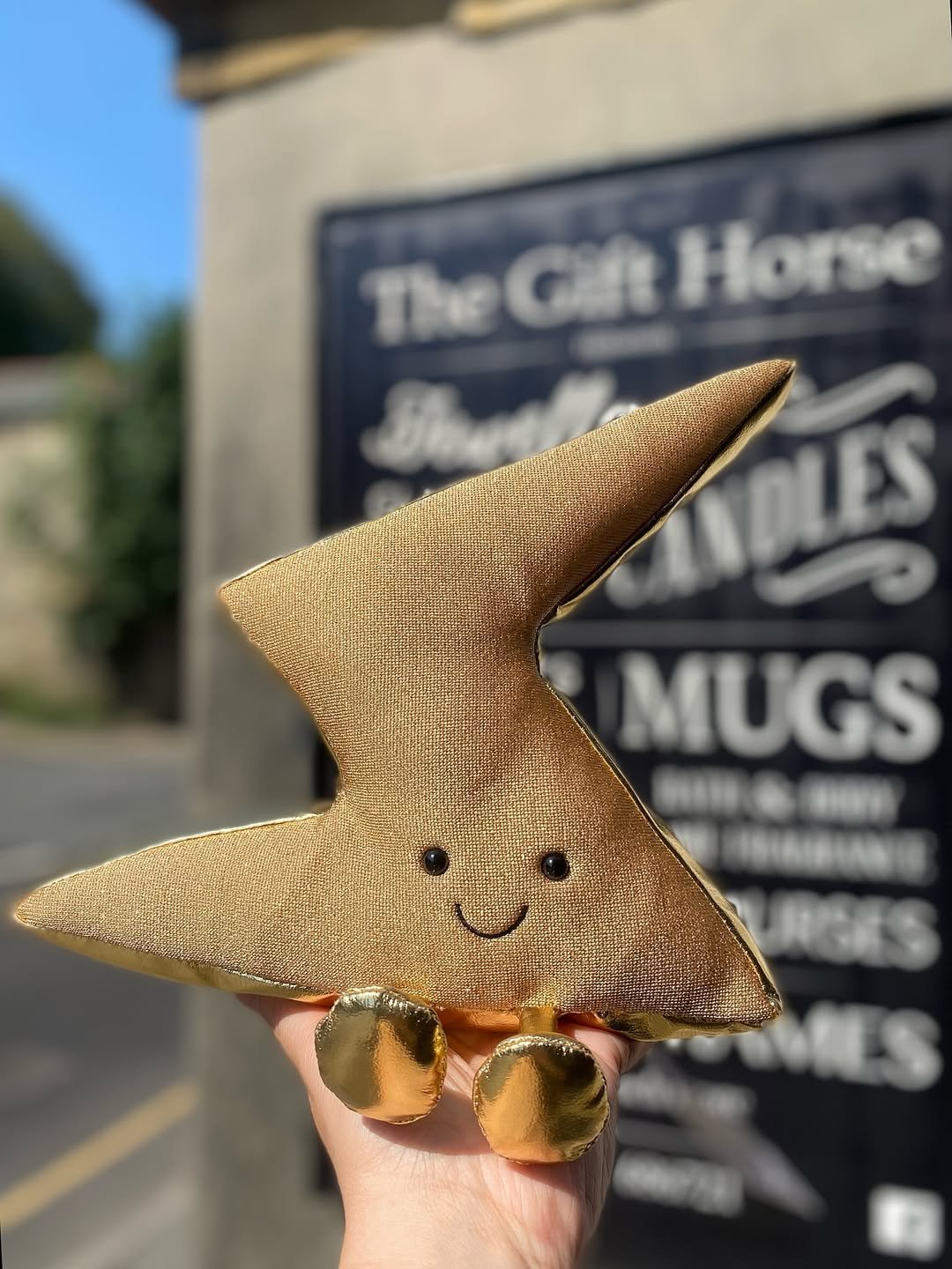 The Gift Horse pavement sign outside the shop on Huddersfield Road, listing candles, mugs, bath and body, and home fragrance, with a gold star soft toy held in front of it.